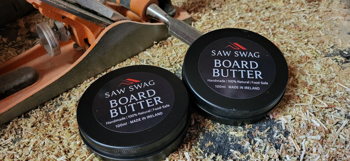 Two containers of Saw Swag Board Butter on a wooden surface with a tool in the background.