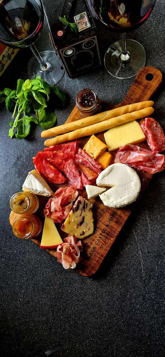 Top-down view of 395mm x 195mm acacia paddle board with handle, styled with cured meats, artisan cheese, breadsticks, and wine