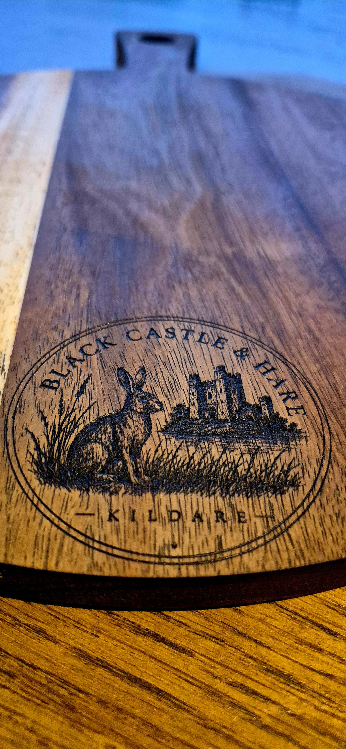 Angled view of artisan pizza board served on a 300mm round acacia wooden pizza board with black castle and hare kildare logo closeup
