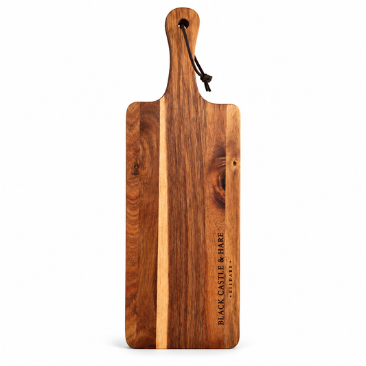 A rectangular wooden serving board with a rounded handle, featuring a dark and light wood grain pattern. The brand name 'BLACK CASTLE & HARE' is engraved vertically on the lower right side, and a dark cord hangs from the handle.