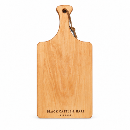 A rectangular wooden serving board with a rounded handle and a hanging loop, shown on a plain white background. The board is light natural wood with the engraved text 'BLACK CASTLE & HARE' and smaller 'KILDARE' at the bottom.
