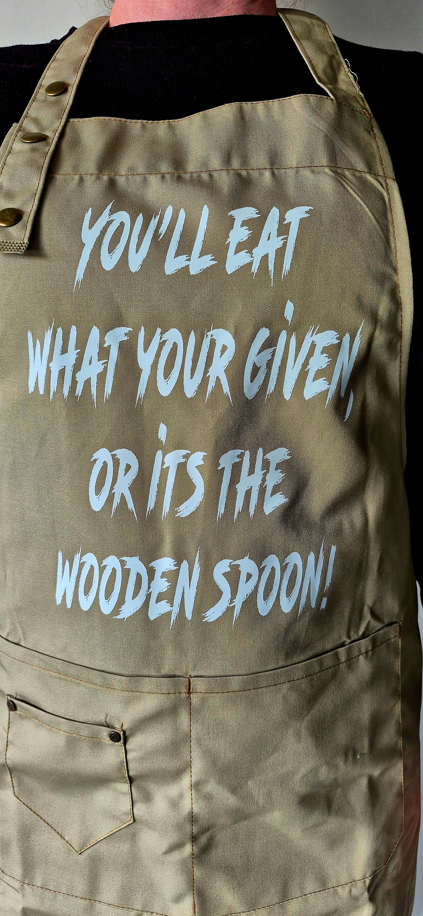 Close up of adjustable neck strap with three metal buttons on khaki apron.