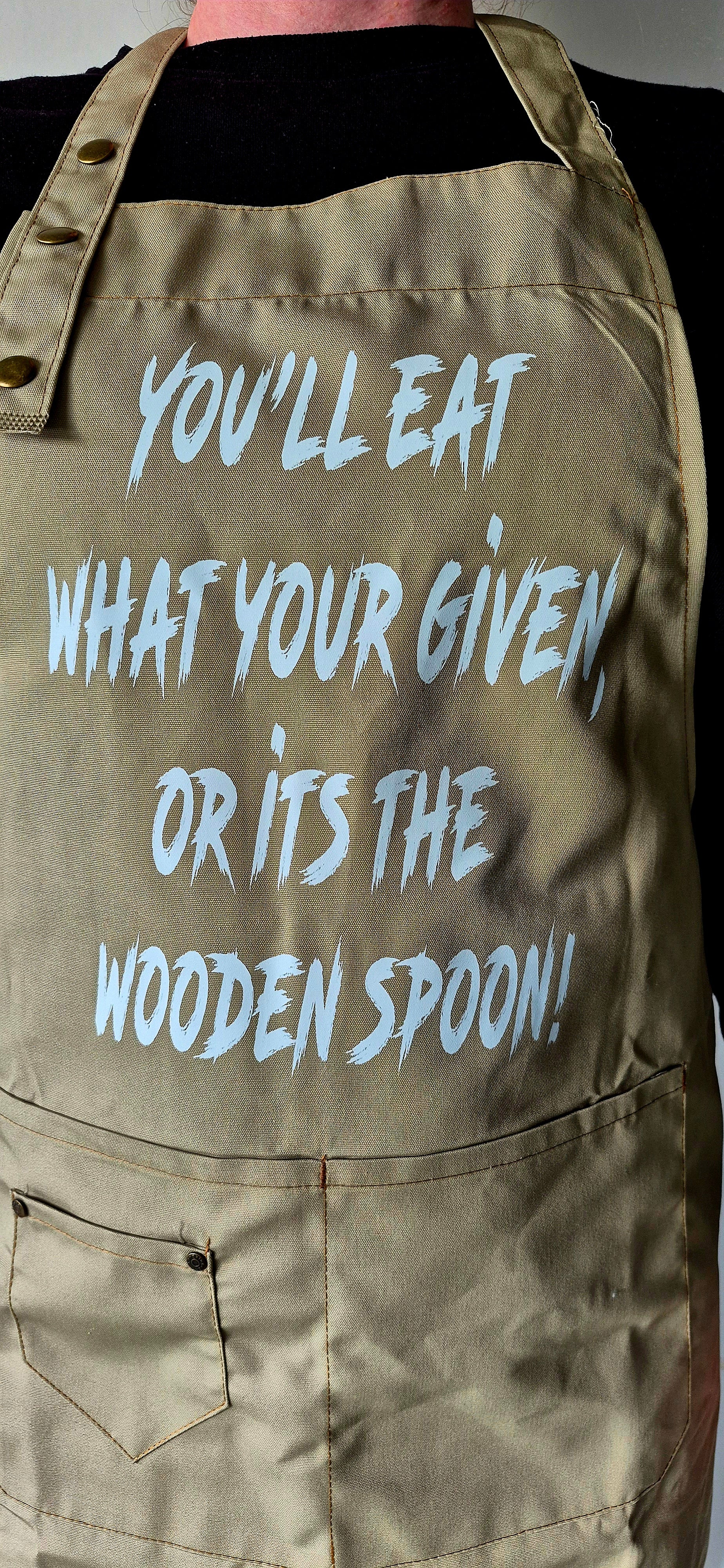 Close up of adjustable neck strap with three metal buttons on khaki apron.