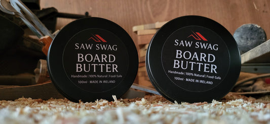 Two containers of Saw Swag Board Butter on a wooden surface with tools in the background.