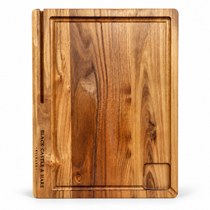 A rectangular wooden serving board with a warm medium-brown wood grain, featuring a raised rim, a vertical slot on the left edge, and the brand name 'BLACK CASTLE & HARE' printed vertically on the left side. A small recessed slot is also present in the bottom right corner.