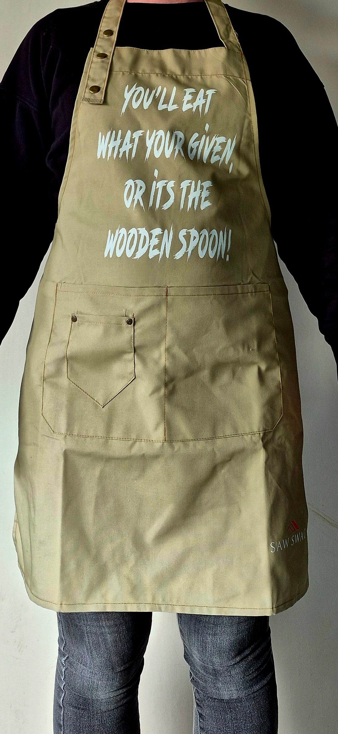 Khaki apron front view showing "Eat what you're given or it's the wooden spoon" text.