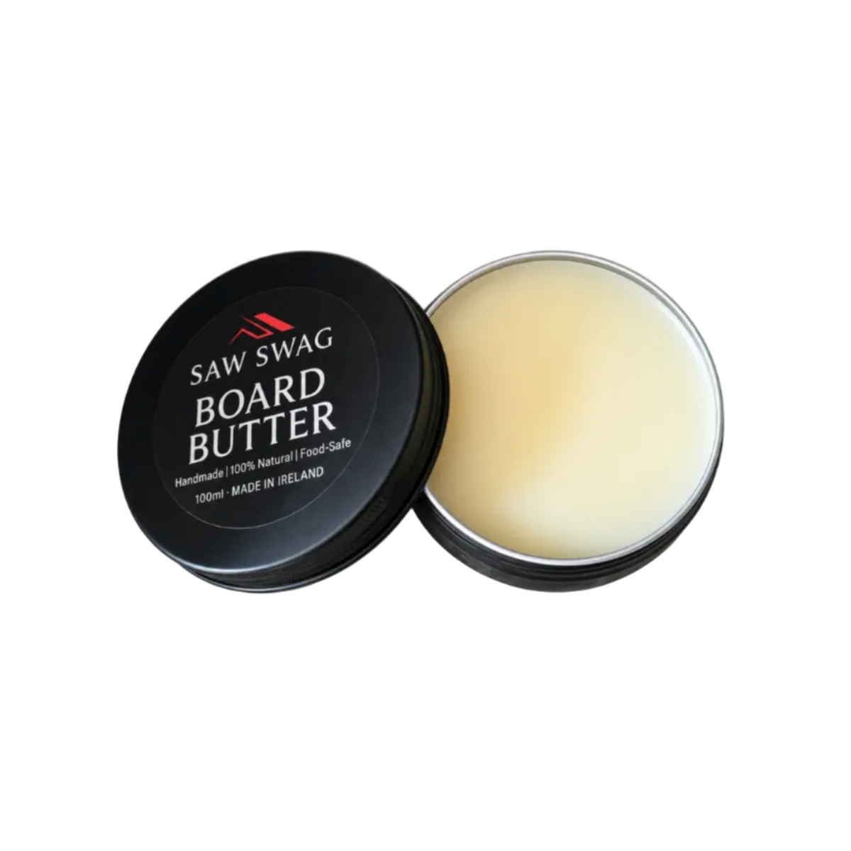 An open round metal tin of Saw Swag Board Butter, showing the pale cream-colored balm inside, with the black lid placed beside it on a white background.