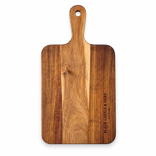 A rectangular wooden cutting board with a rounded handle and a hanging hole, featuring a vertical grain pattern and the engraved brand name 'BLACK CASTLE & HARE LONDON' on the right side, shown against a plain white background.