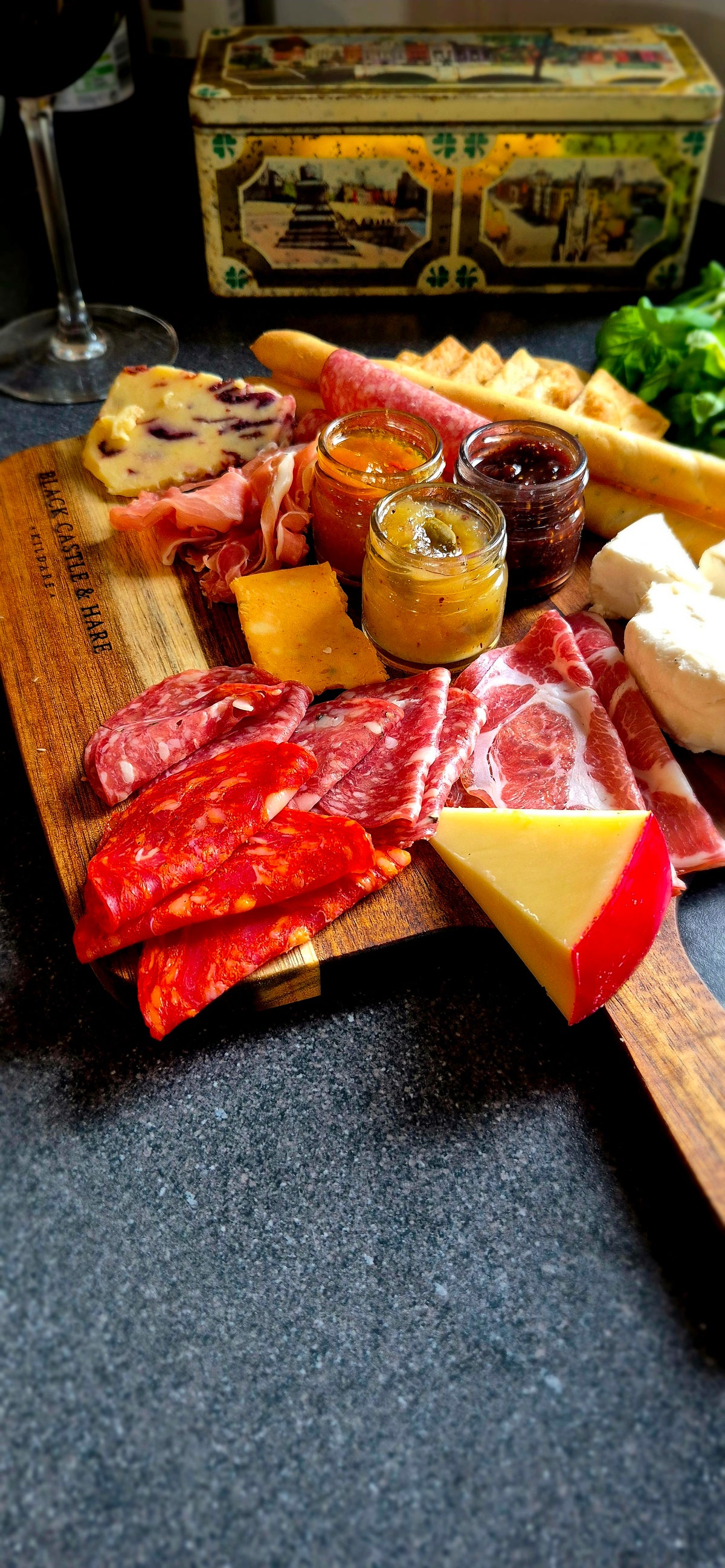 Angled view of double-oiled 350mm x 250mm x 15mm acacia serving board styled with cured meat, cheese, and red wine background