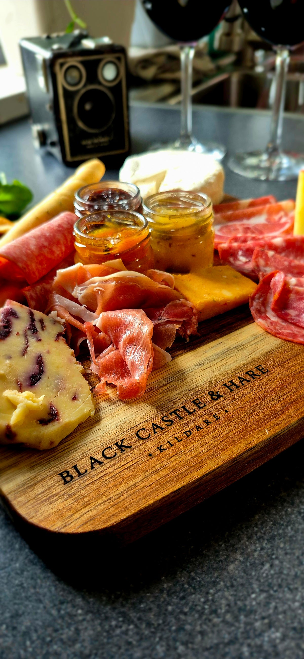 10-person acacia wood charcuterie board featuring meats, cheeses, and breadsticks paired with glasses of wine