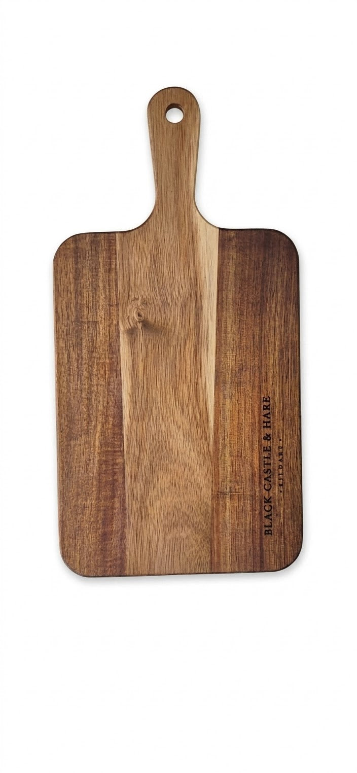 A rectangular wooden serving board with rounded corners and a handle, shown on a plain white background. The board features a vertical grain pattern with alternating medium and dark brown wood tones, and the brand name 'BLACK CASTLE & HARE' is printed vertically on the lower right side.