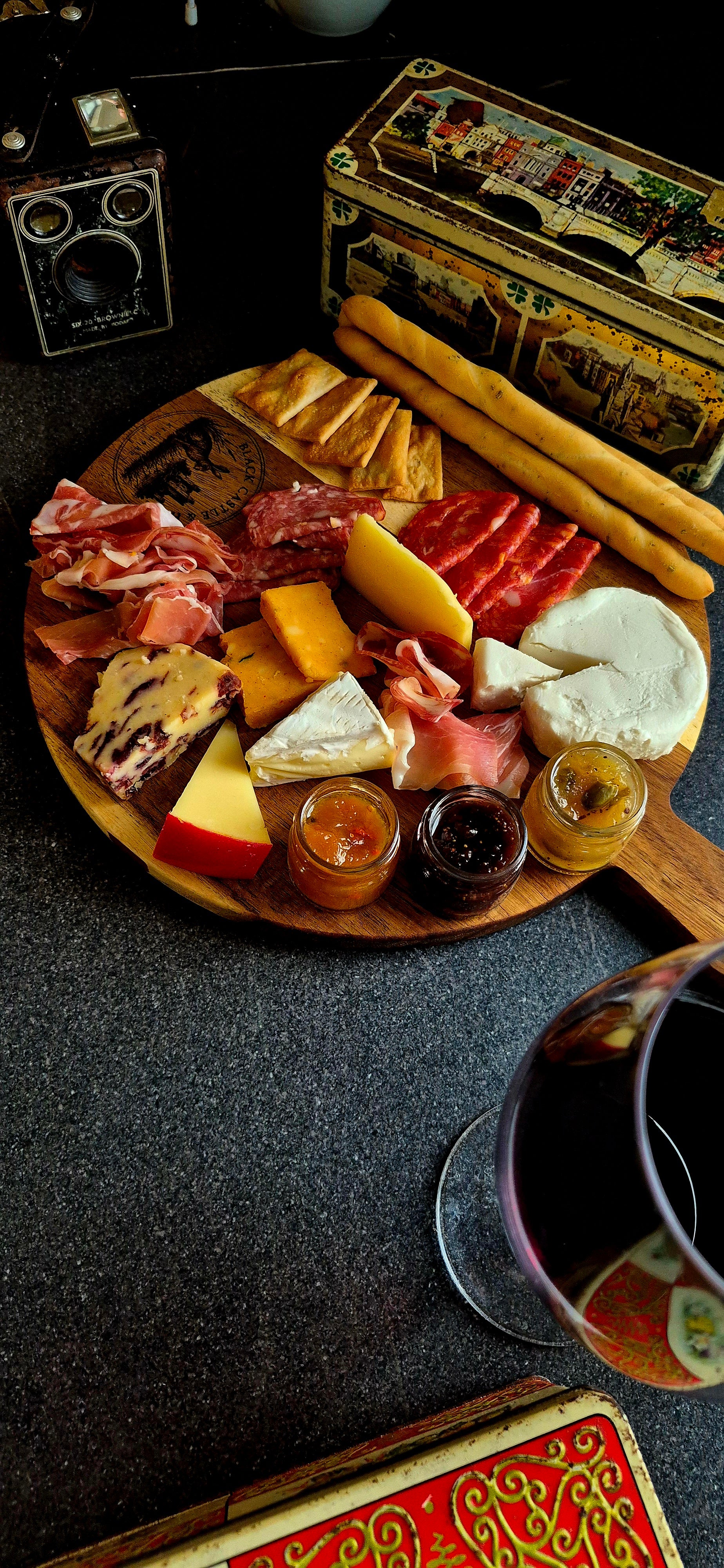 Round acacia wood charcuterie board with 100mm handle styled with artisan cheeses, salami, and crispy breadsticks next to wine