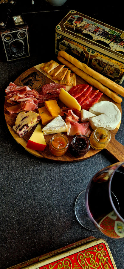 Round acacia wood charcuterie board with 100mm handle styled with artisan cheeses, salami, and crispy breadsticks next to wine