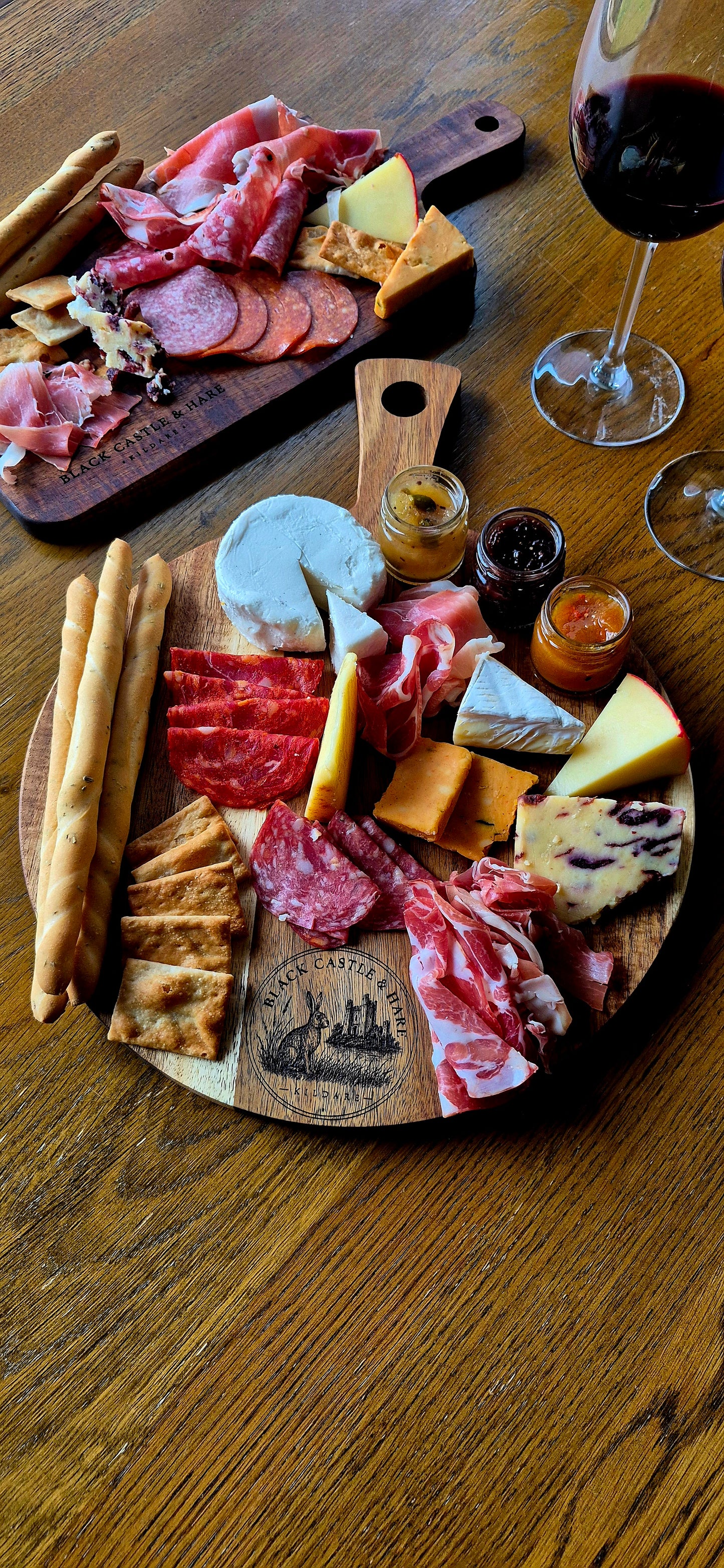 Full table setting with a 300mm round acacia wood dual-use pizza and charcuterie board with breadsticks, cheeses, meats, and wine
