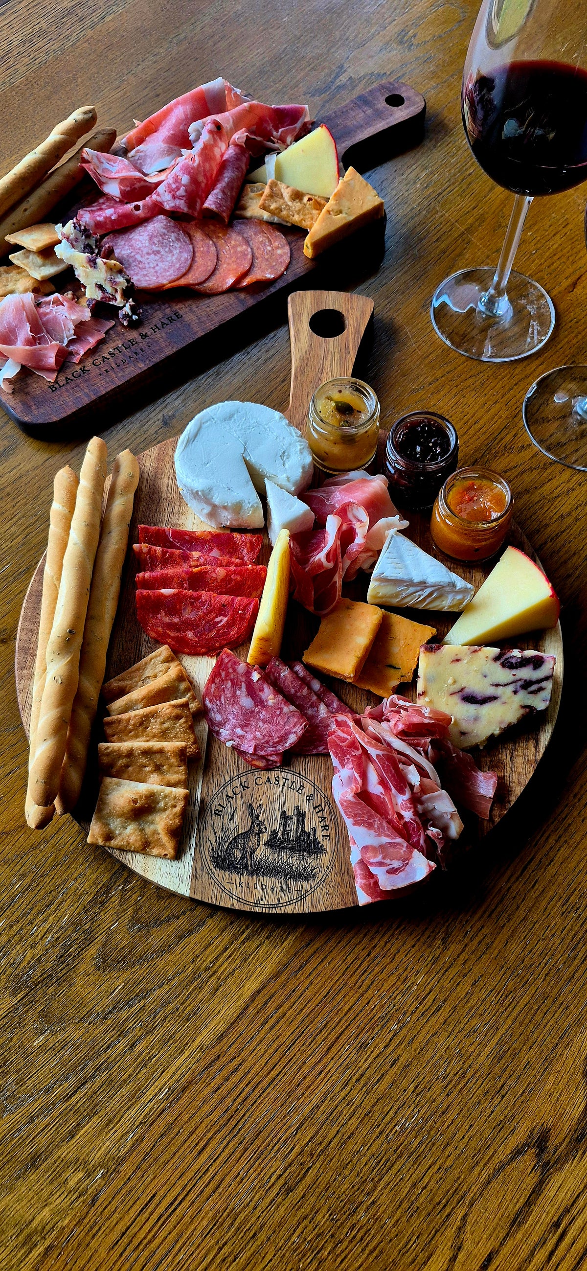Full table setting with a 300mm round acacia wood dual-use pizza and charcuterie board with breadsticks, cheeses, meats, and wine