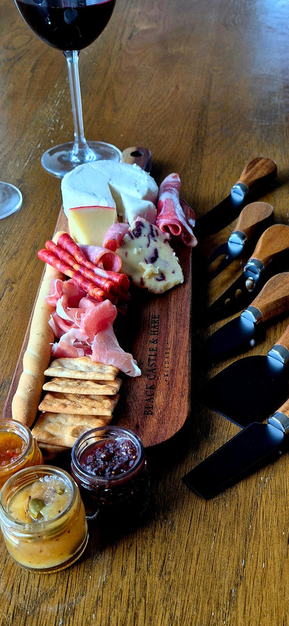 Side-angle shot of double-oiled personal acacia wood charcuterie platter with breadsticks, gourmet cheese, and red wine background.