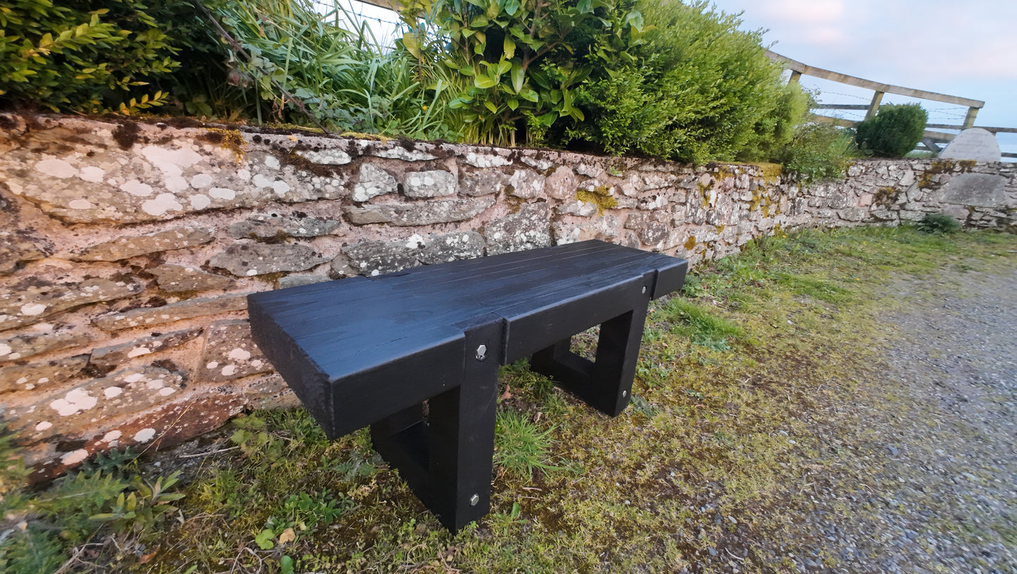 Solid heavy-duty outdoor wooden bench finished in Black Ash sitting in front of an old irish wall