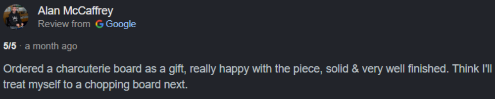 A screenshot of a Google Reviews review card showing a customer named Alan McCaffrey giving a 1-star review. The review text says they ordered a charcuterie board as a gift, expressed happiness with the piece, and plans to buy a chopping board next.