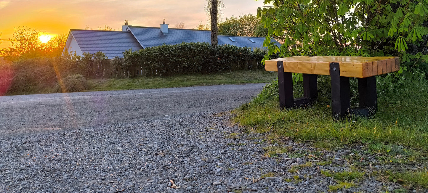 Solid heavy-duty outdoor wooden bench with a natural seat finish sitting under a large tree at sunset
