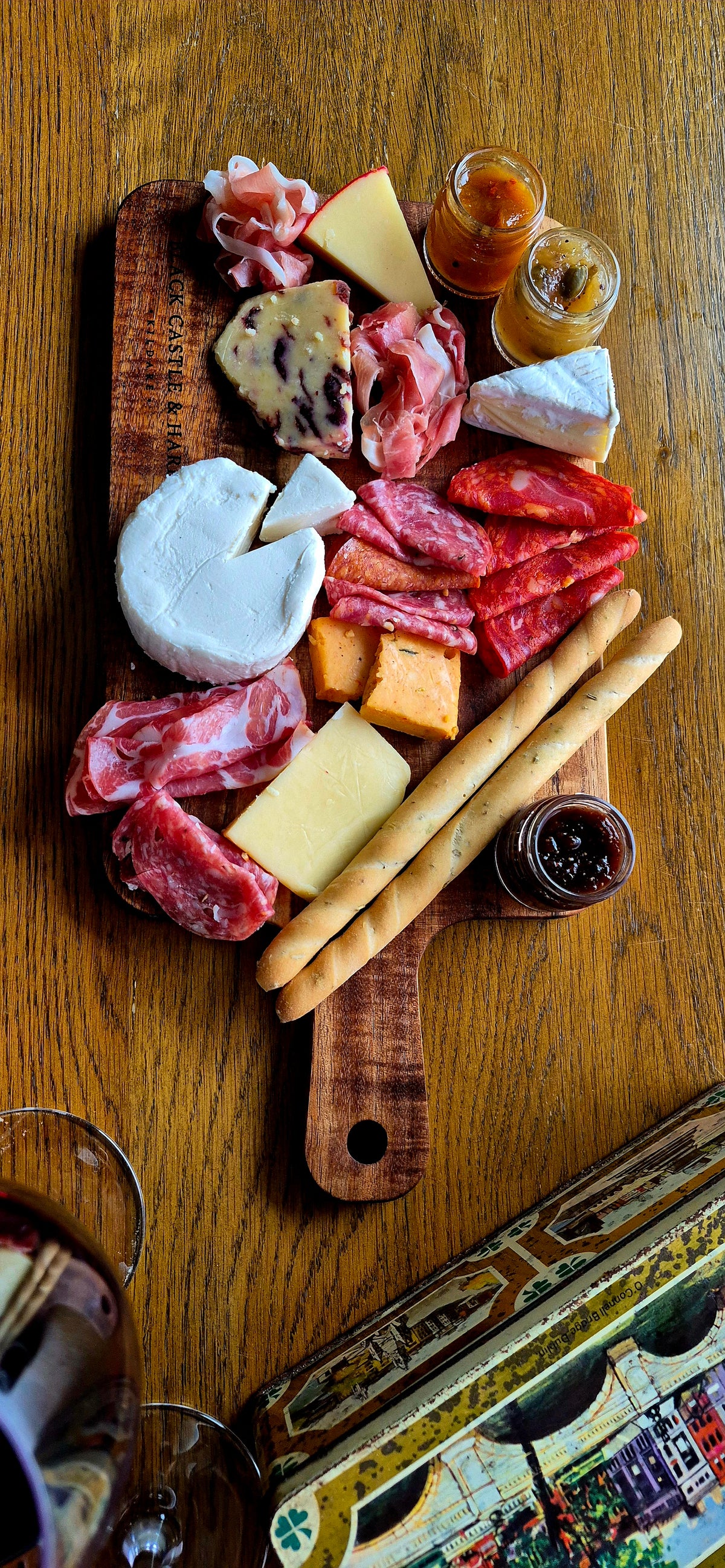 Top-down view of 395mm x 195mm acacia paddle board with handle, styled with cured meats, artisan cheese, breadsticks, and wine