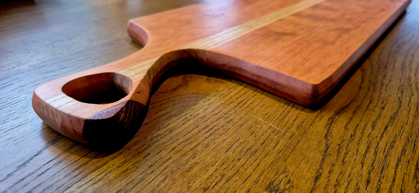 A handcrafted serving board featuring a central Oak panel wrapped in a Cherry wood frame with a dark Walnut handle accent