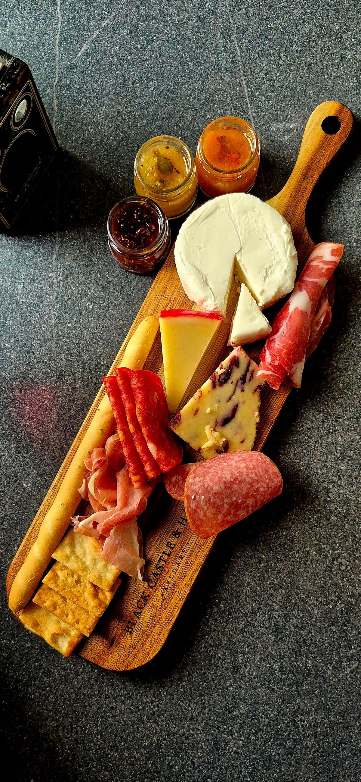 Top-down view of a personal wooden charcuterie board loaded with cured meats, cheeses, and breadsticks paired with glasses of wine.