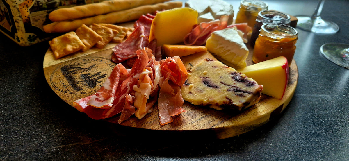 Top-down view of 300mm round acacia board used for charcuterie, filled with cured meats, cheeses, breadsticks, and wine