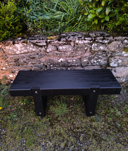 Black Ash wooden bench against an old stone wall with greenery