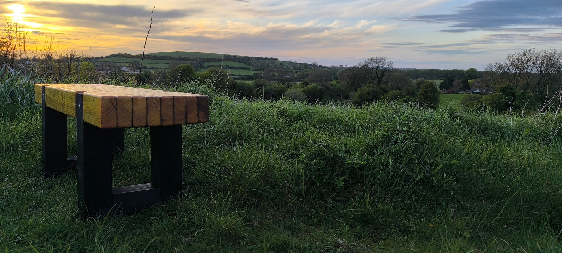 Wooden bench in a grassy field with a sunset or sunrise in the background