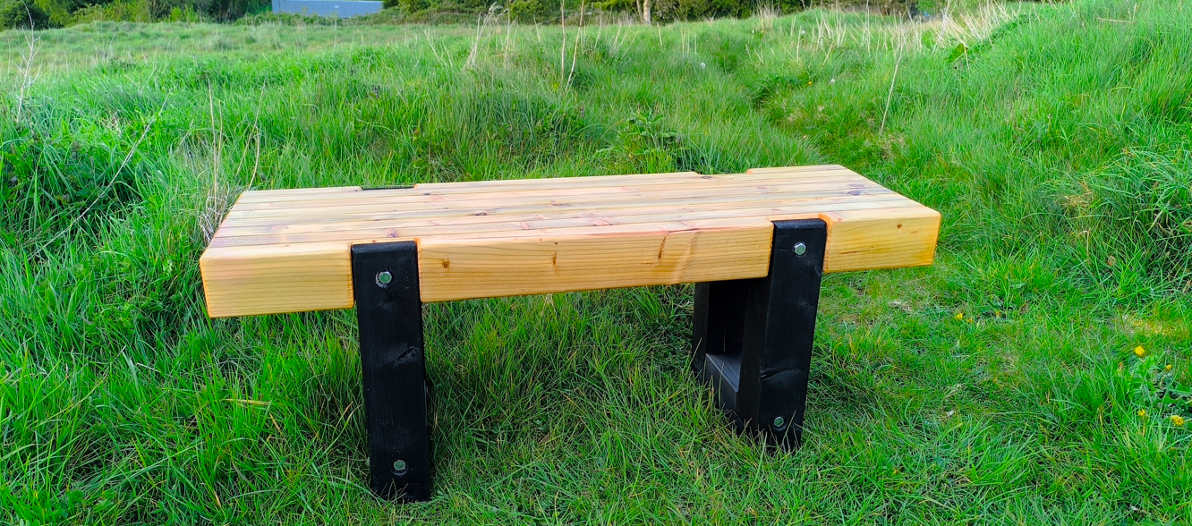 Wooden bench with black wooden legs in a grassy field